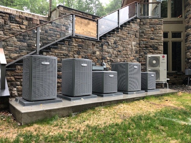 Five residential AC condenser units installed on a concrete pad against a stone wall, Dallas-Fort Worth